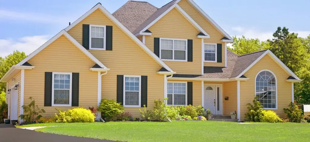 A sunlit two-story home in yellow lap siding with black shutters and a full front lawn